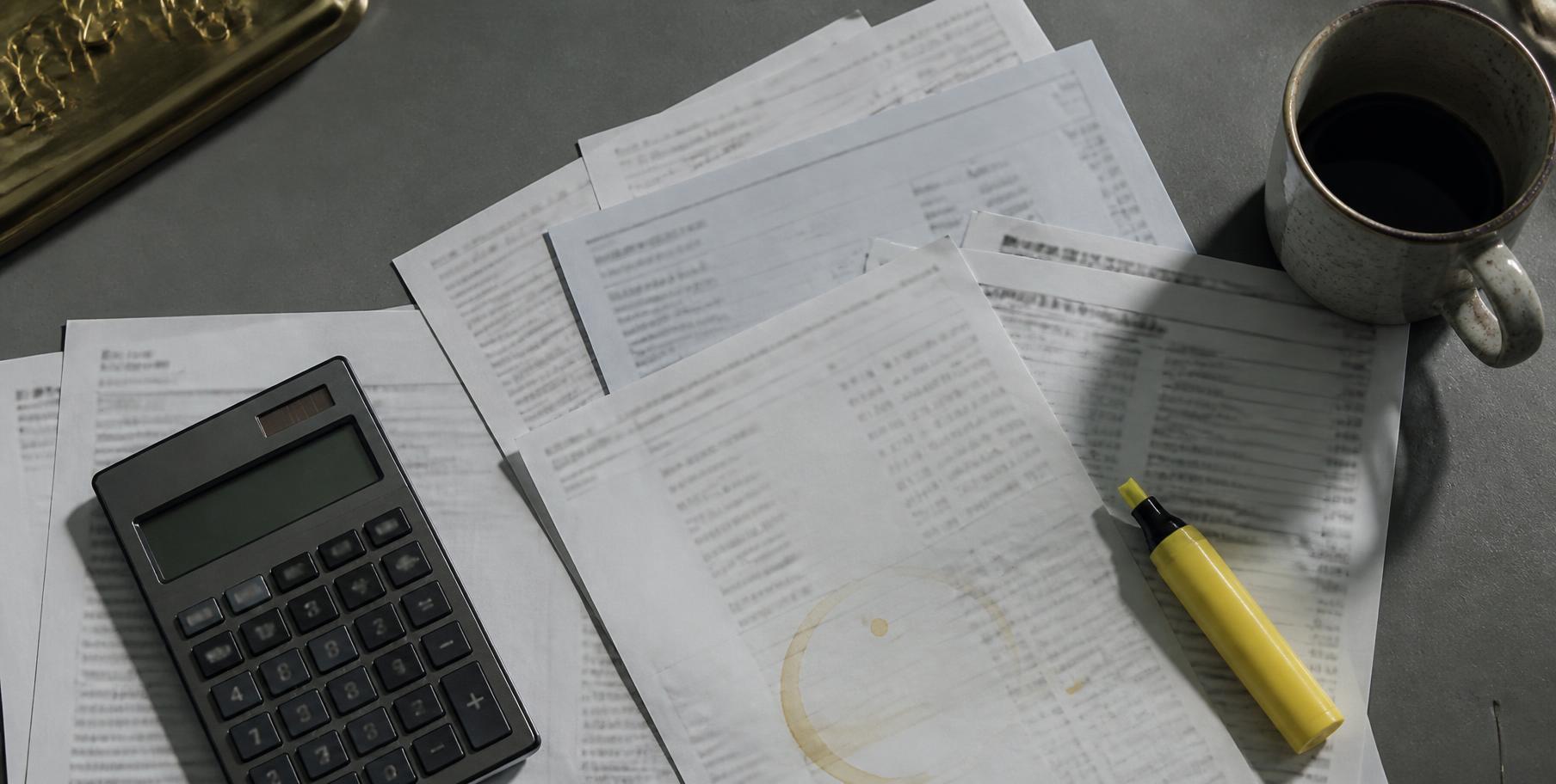 Tax returns and bank statements fanned out beside a calculator and highlighter