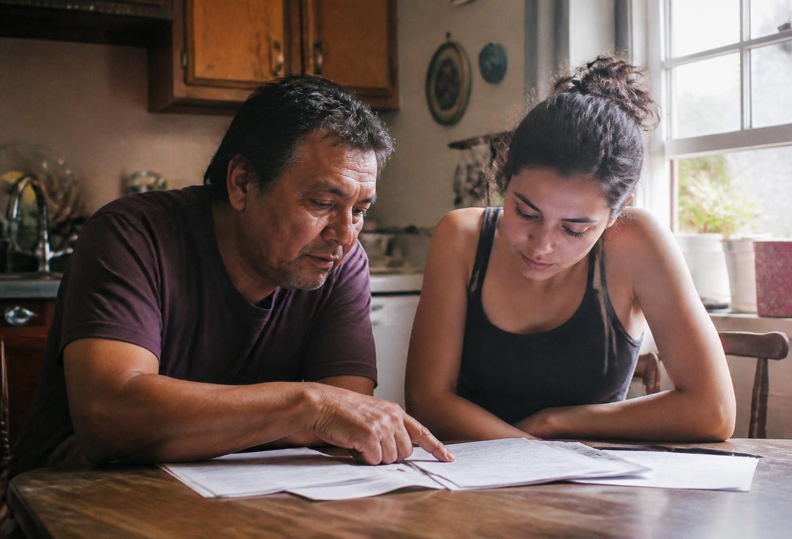 A sponsor and a family member reading sponsorship paperwork together at a kitchen table