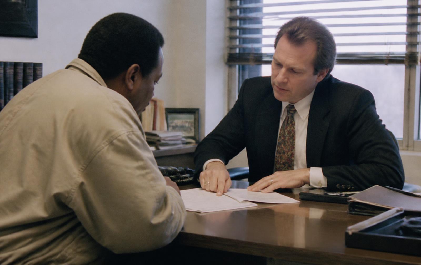 A client and lawyer reviewing printed forms across a desk