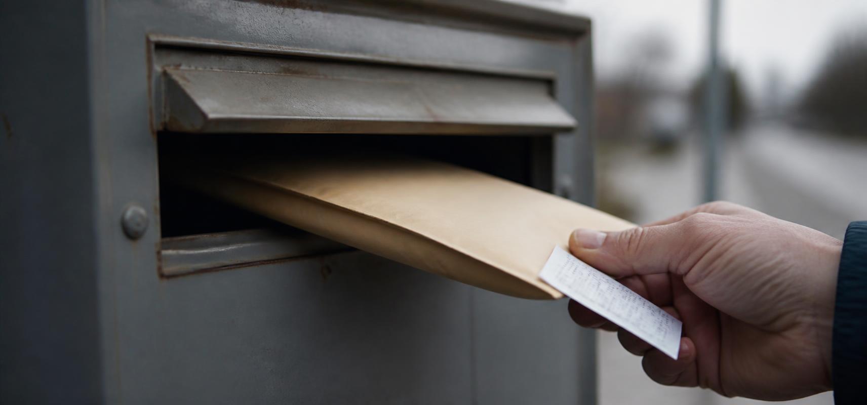 A hand posting a business envelope with a certified-mail receipt
