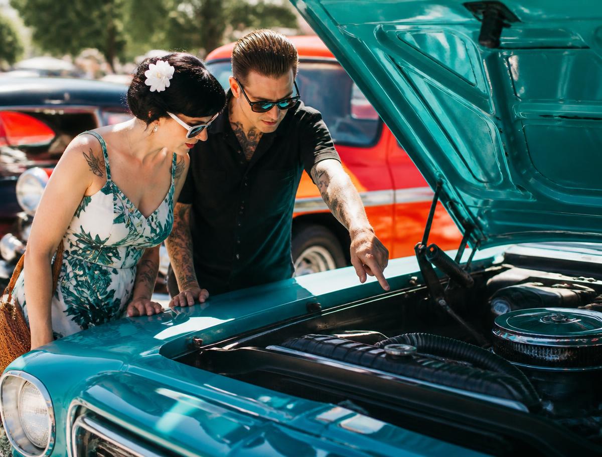 A seller and buyer shaking hands beside a car in a driveway